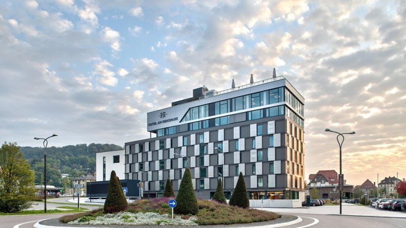 Modernes Hotelgeb&auml;ude mit Glasfassade, umgeben von einem Kreisverkehr und gepflegter Landschaftsgestaltung, bei Sonnenuntergang., &copy; Hotel am Remspark