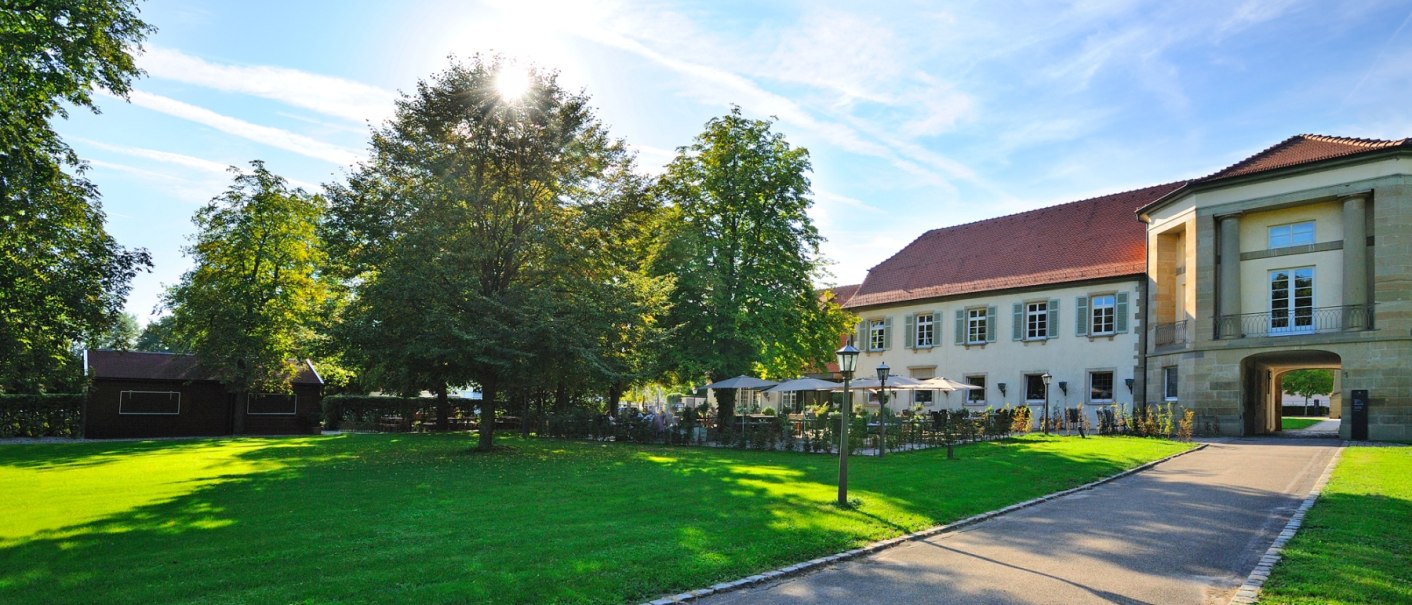 Elegantes Gebäude mit Terrasse und Sonnenschirmen, umgeben von grüner Wiese und Bäumen bei sonnigem Wetter., © Schlosshotel Monrepos Elegantes Gebäude mit Terrasse und Sonnenschirmen, umgeben von grüner Wiese und Bäumen bei sonnigem Wetter., © Schlosshotel Monrepos