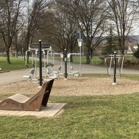 Ein Outdoor-Fitnessbereich mit verschiedenen Trainingsger&auml;ten und einer Holzbank in einem Park. Die Umgebung ist von B&auml;umen umgeben., &copy; cStadtN&uuml;rtingen
