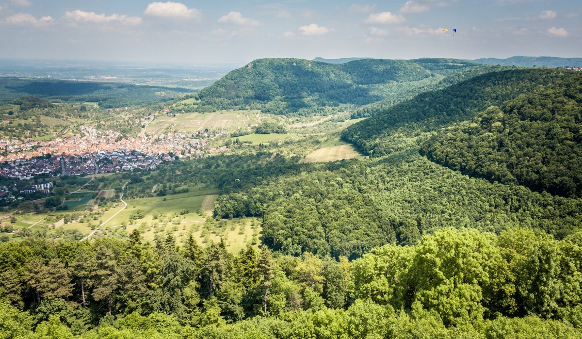 Blick von der Burg Hohenneuffen auf das Dorf Beuren, umgeben von grünen Wäldern und Hügeln unter einem blauen Himmel mit wenigen Wolken., © hochgehberge