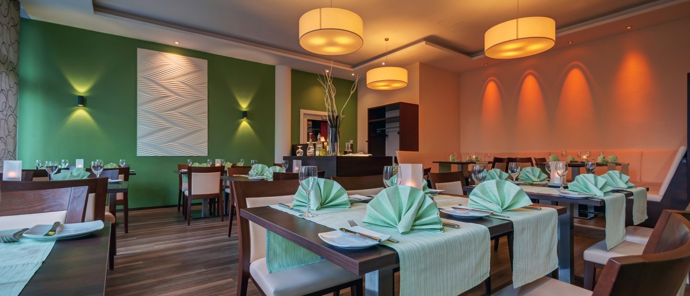 Elegantes Restaurant mit grünen Tischdecken, stilvoller Beleuchtung und moderner Wanddekoration. Die Atmosphäre wirkt einladend und gepflegt., © City Hotel Reutlingen