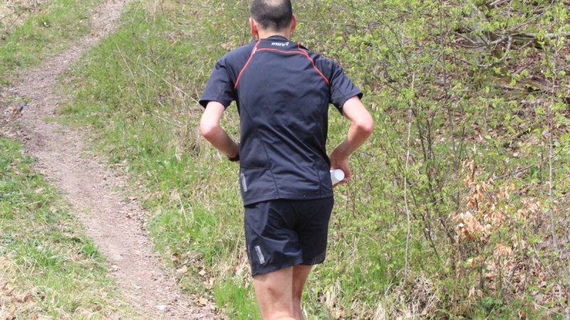 Ein Trailläufer in schwarzer Sportkleidung joggt auf einem schmalen Pfad durch einen grünen Wald., © Natur.Nah. Schönbuch & Heckengäu