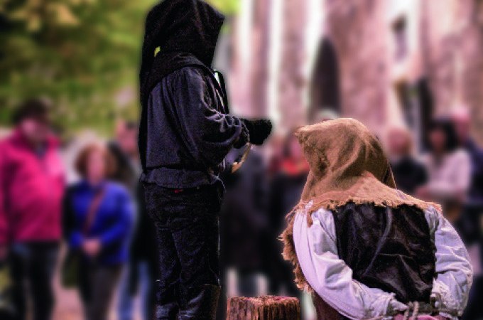Mittelalterliche Szene mit zwei Personen in historischer Kleidung, eine kniet vor einem Holzblock, während die andere daneben steht. Zuschauer im Hintergrund., © Esslinger Stadtmarketing &amp; Tourismus GmbH