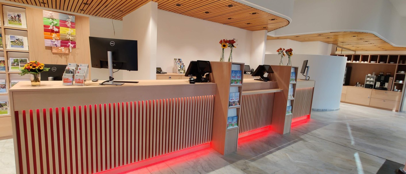 Moderner Empfangsbereich mit Holztheke, Computern, Broschüren und Blumenvasen. Helle Beleuchtung und stilvolle Einrichtung., © Larissa Philipp Moderner Empfangsbereich mit Holztheke, Computern, Broschüren und Blumenvasen. Helle Beleuchtung und stilvolle Einrichtung., © Larissa Philipp