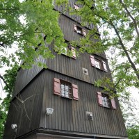 Hoher Holzturm mit roten Fensterläden, umgeben von grünen Bäumen. Der Turm hat eine steinerne Basis und ist von unten nach oben fotografiert., © Land der 1000 Hügel - Kraichgau-Stromberg Hoher Holzturm mit roten Fensterläden, umgeben von grünen Bäumen. Der Turm hat eine steinerne Basis und ist von unten nach oben fotografiert., © Land der 1000 Hügel - Kraichgau-Stromberg