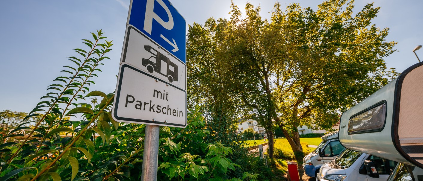 Ein Schild f&uuml;r einen Wohnmobilstellplatz mit Parkschein, umgeben von B&auml;umen und geparkten Wohnmobilen bei sonnigem Wetter., &copy; Stuttgart-Marketing GmbH, Thomas Niederm&uuml;ller