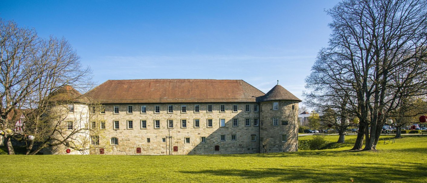 Das Burgschloss in Schorndorf, umgeben von grüner Wiese und kahlen Bäumen unter klarem blauem Himmel., © SMG, Sarah Schmid Das Burgschloss in Schorndorf, umgeben von grüner Wiese und kahlen Bäumen unter klarem blauem Himmel., © SMG, Sarah Schmid