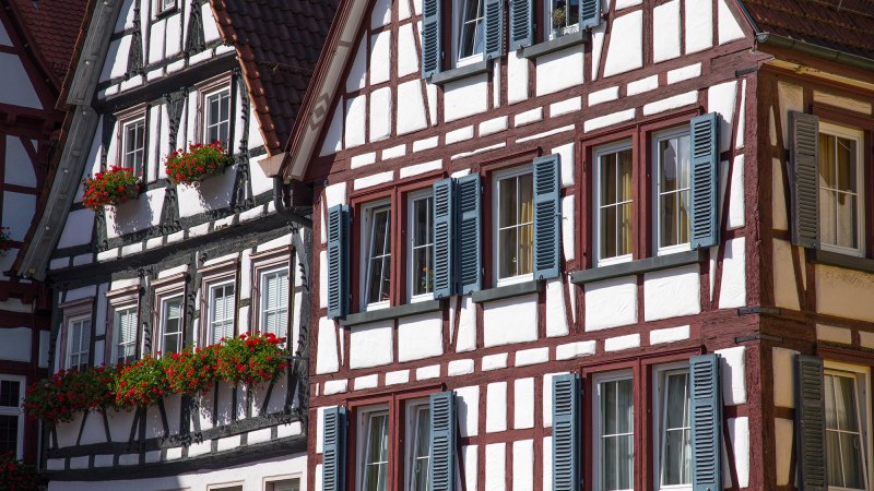 Fachwerkhäuser mit blauen Fensterläden und roten Blumen in den Blumenkästen, bei Tageslicht aufgenommen., © Bad Urach Tourismus