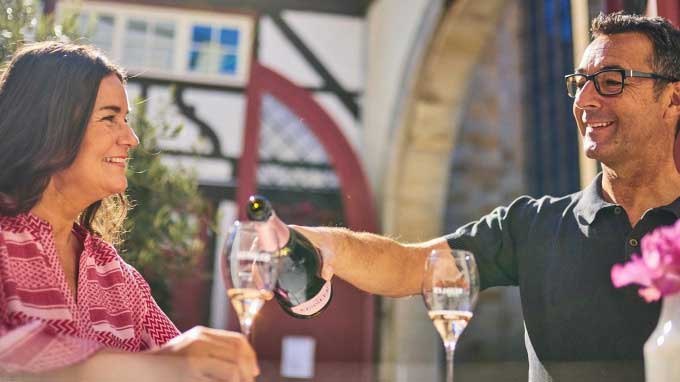Ein Paar genie&szlig;t Sekt im Freien vor einem Fachwerkhaus. Der Mann schenkt der Frau ein Glas ein, w&auml;hrend sie l&auml;chelt., &copy; Esslinger Stadtmarketing & Tourismus GmbH