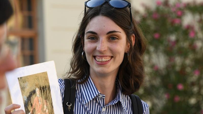Frau mit gestreiftem Hemd und Sonnenbrille auf dem Kopf h&auml;lt ein Bild in der Hand, l&auml;chelnd vor unscharfem Hintergrund., &copy; &copy; G&uuml;nter Kreft