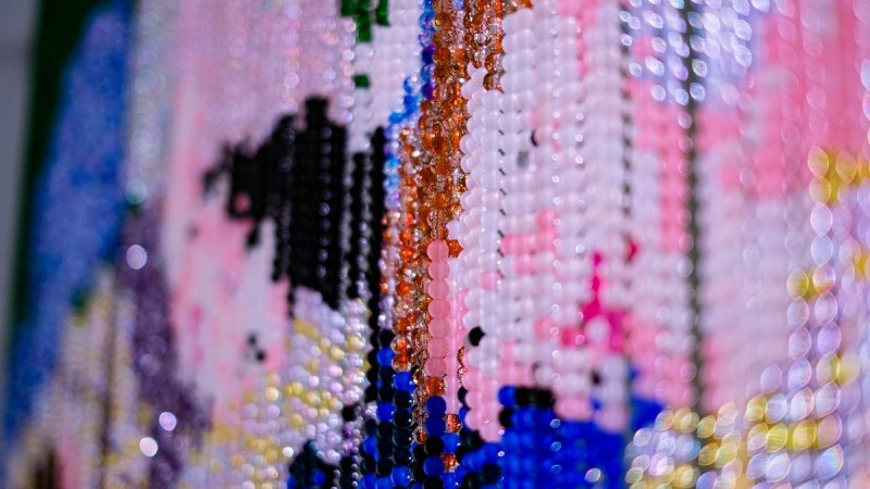 Detailaufnahme eines Kunstwerks aus bunten Perlen, die ein abstraktes Muster formen. Farben wie Rosa, Blau und Schwarz dominieren., © Mizi Lee, Also jetzt siehst Du mich, 2024. (Detail)