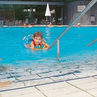 Ein Kind im Schwimmring im Pool, Erwachsene schwimmen und entspannen auf Liegestühlen im Badhaus Bad Boll., © Stuttgart-Marketing GmbH