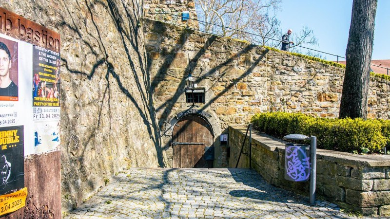 Eingang zur Club Bastion in Kirchheim unter Teck, umgeben von alten Steinmauern. Plakate f&uuml;r Veranstaltungen sind an der Wand angebracht., &copy; Stuttgart-Marketing GmbH, Sarah Schmid
