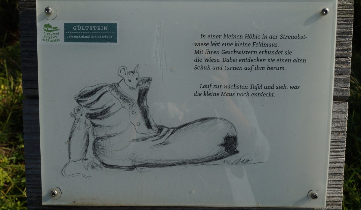 Infotafel mit einer Zeichnung einer Maus in einem Schuh. Text beschreibt das Abenteuer einer kleinen Feldmaus auf einer Streuobstwiese., © Natur.Nah. Schönbuch & Heckengäu Infotafel mit einer Zeichnung einer Maus in einem Schuh. Text beschreibt das Abenteuer einer kleinen Feldmaus auf einer Streuobstwiese., © Natur.Nah. Schönbuch & Heckengäu