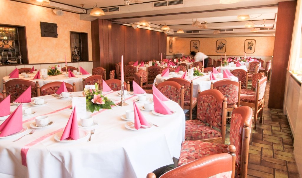 Festlich gedeckte Tische in einem Restaurant mit rosa Servietten, Blumenarrangements und gedecktem Geschirr für eine Familienfeier., © Ulli Kellenbenz Festlich gedeckte Tische in einem Restaurant mit rosa Servietten, Blumenarrangements und gedecktem Geschirr für eine Familienfeier., © Ulli Kellenbenz