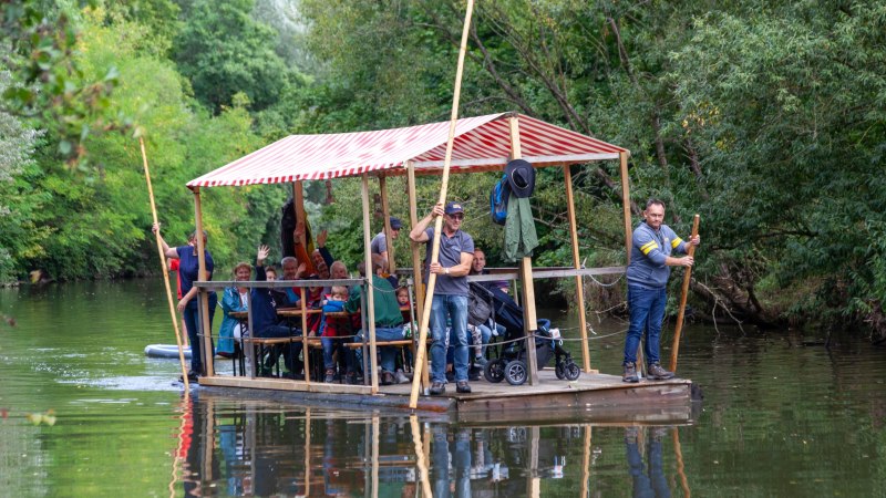 überdachtes Holzfloß mit Menschen auf dem Fluß, an den Ufern Büsche und Bäume, © Stadt Gaildorf