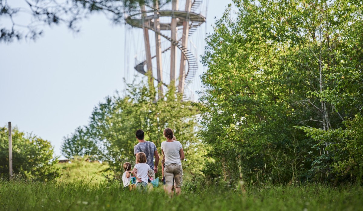 Eine Familie spaziert durch einen grünen Park. Im Hintergrund ist ein hoher Aussichtsturm zu sehen, umgeben von Bäumen., © Natur.Nah. Schönbuch & Heckengäu Eine Familie spaziert durch einen grünen Park. Im Hintergrund ist ein hoher Aussichtsturm zu sehen, umgeben von Bäumen., © Natur.Nah. Schönbuch & Heckengäu