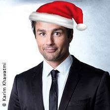 Person in Anzug mit Weihnachtsmütze, lächelnd vor neutralem Hintergrund., © links im Bild