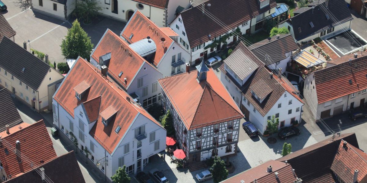 Luftaufnahme eines Dorfes mit Fachwerkhäusern und roten Dächern. Im Zentrum ein Gebäude mit rotem Dach und Sonnenschirmen., © Hotel Gasthof Lamm Luftaufnahme eines Dorfes mit Fachwerkhäusern und roten Dächern. Im Zentrum ein Gebäude mit rotem Dach und Sonnenschirmen., © Hotel Gasthof Lamm