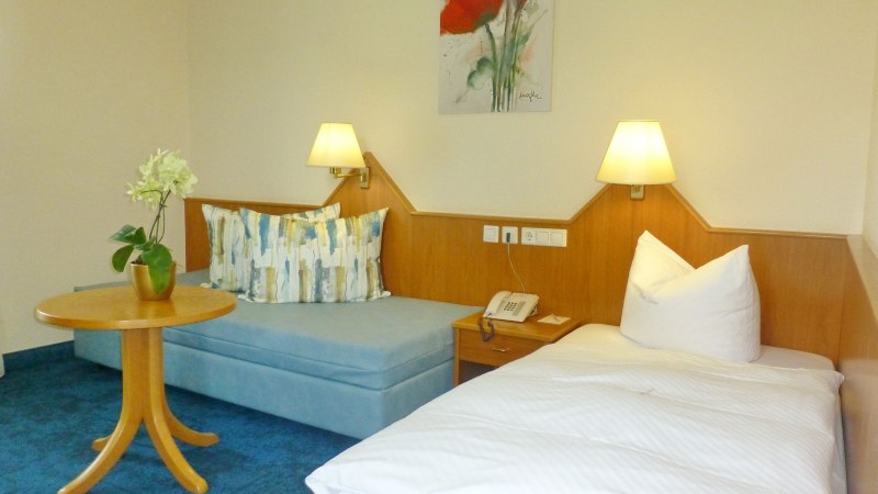 Ein gemütliches Einzelzimmer mit einem Bett, einem kleinen Sofa, einem runden Holztisch und einer Tischlampe. An der Wand hängt ein Blumenbild., © Hotel & Restaurant Sonne