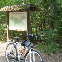Ein Fahrrad steht vor einer Informationstafel im Naturpark Sch&ouml;nbuch. Der Wald im Hintergrund ist dicht und gr&uuml;n., &copy; Natur.Nah. Sch&ouml;nbuch & Heckeng&auml;u