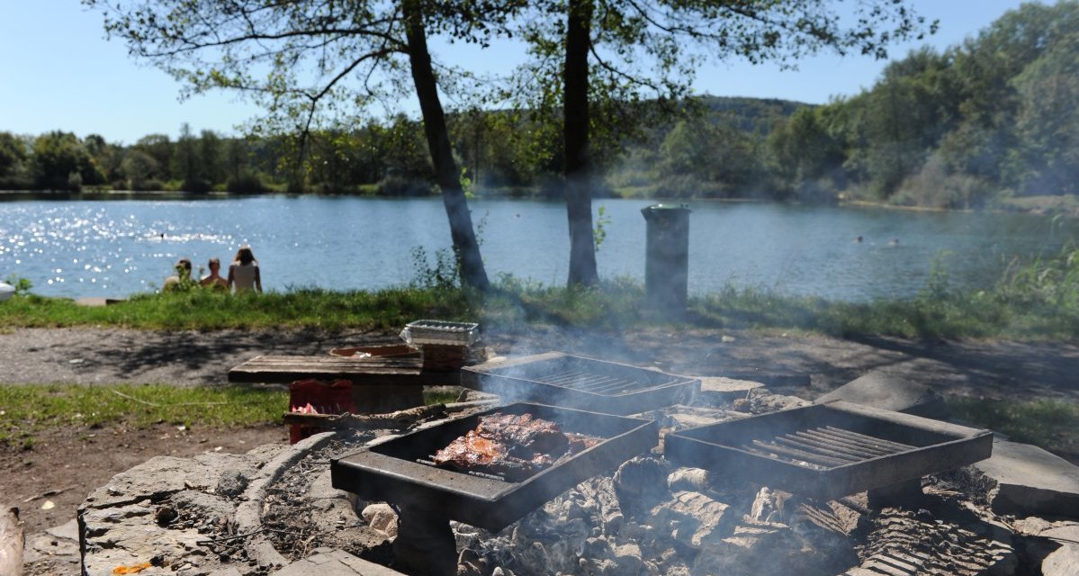 Grillstelle mit Fleisch am Seeufer, im Hintergrund Menschen am Wasser. Bäume und blauer Himmel umrahmen die Szene., © Land der 1000 Hügel - Kraichgau-Stromberg Grillstelle mit Fleisch am Seeufer, im Hintergrund Menschen am Wasser. Bäume und blauer Himmel umrahmen die Szene., © Land der 1000 Hügel - Kraichgau-Stromberg