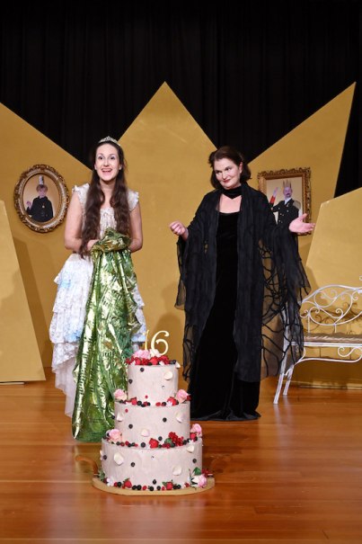 Zwei Frauen in einem Märchenmusical, eine in einem weißen Kleid mit Krone, die andere in einem schwarzen Umhang, stehen hinter einer großen Torte., © Stadtverwaltung Kirchheim unter Teck - Kulturring Zwei Frauen in einem Märchenmusical, eine in einem weißen Kleid mit Krone, die andere in einem schwarzen Umhang, stehen hinter einer großen Torte., © Stadtverwaltung Kirchheim unter Teck - Kulturring