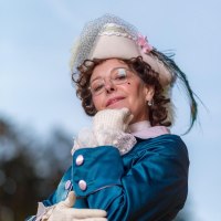 Eine Frau in historischer Kleidung mit einem verzierten Hut und Brille posiert selbstbewusst vor einem blauen Himmel., &copy; Quelle: Irma Beck