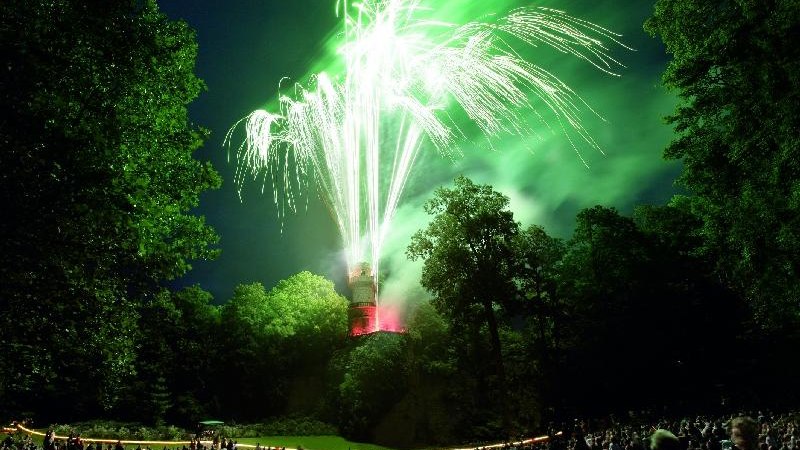 Ein spektakuläres Feuerwerk erleuchtet den Nachthimmel über einem Turm, umgeben von Bäumen und einer großen Menschenmenge in einem Park., © copyright: Marc Sansone Ein spektakuläres Feuerwerk erleuchtet den Nachthimmel über einem Turm, umgeben von Bäumen und einer großen Menschenmenge in einem Park., © copyright: Marc Sansone
