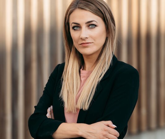 Frau mit langen blonden Haaren und schwarzem Blazer steht selbstbewusst vor einer Holzwand., &copy; Dieselstrasse Kulturzentrum e.V.