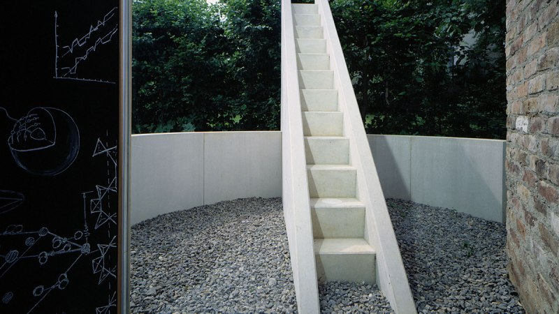 Weiße Treppe in rundem Kiesbereich, umgeben von Bäumen. Links Tafel mit Zeichnungen., © TOMAS
