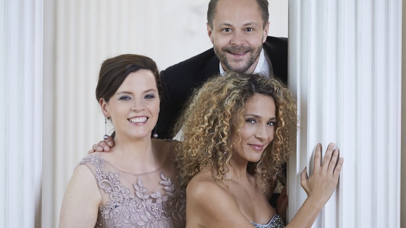 Drei elegant gekleidete Personen l&auml;cheln vor wei&szlig;en S&auml;ulen. Sie tragen Abendgarderobe und wirken fr&ouml;hlich und stilvoll., &copy; Touristik Bad Wildbad GmbH