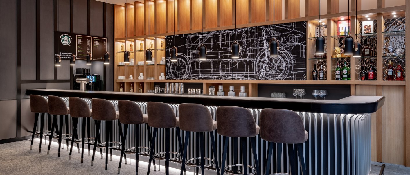 Moderne Bar mit hohen Stühlen, beleuchteten Regalen und einer Tafel mit technischen Zeichnungen im Hintergrund., © copyright by Kilian Blees Moderne Bar mit hohen Stühlen, beleuchteten Regalen und einer Tafel mit technischen Zeichnungen im Hintergrund., © copyright by Kilian Blees