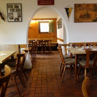 Ein gemütliches Restaurant mit Holztischen und -stühlen, dekoriert mit Bildern und Blumen. Ein Bogen führt in einen weiteren Raum., © Besenwirtschaft Familie Nerz