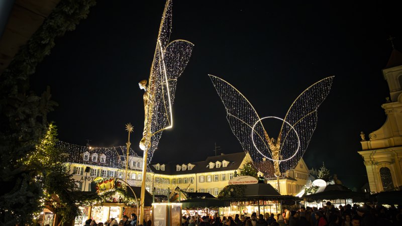 Der Ludwigsburger Barock-Weihnachtsmarkt auf dem Marktplatz bei Nacht, beleuchtete große Engelsfiguren und Buden. Einige Besucherinnen und Besucher tummeln sich auf dem Platz., © Stuttgart Marketing GmbH, Sarah Schmid