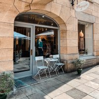 Ein kleines Ladengesch&auml;ft mit Schaufenster, dekoriert mit Kleidung. Davor stehen zwei wei&szlig;e St&uuml;hle und ein Tisch auf dem Gehweg., &copy; MAGASIN Gei&szlig;strasse 15, Stuttgart