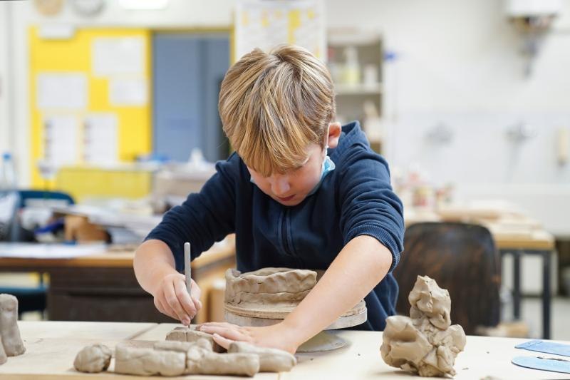 Ein Junge arbeitet konzentriert an einer Tonfigur in einem Workshop. Er trägt einen blauen Pullover und sitzt an einem Tisch mit Tonmaterialien., © Kunstschule Labyrinth