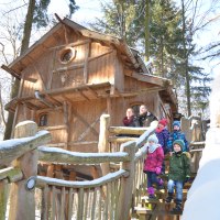 Eine Familie steht auf der Treppe eines verschneiten Baumhauses im Wald. Das Holzhaus ist rustikal und von B&auml;umen umgeben., &copy; Tripsdrill Natur-Resort GmbH