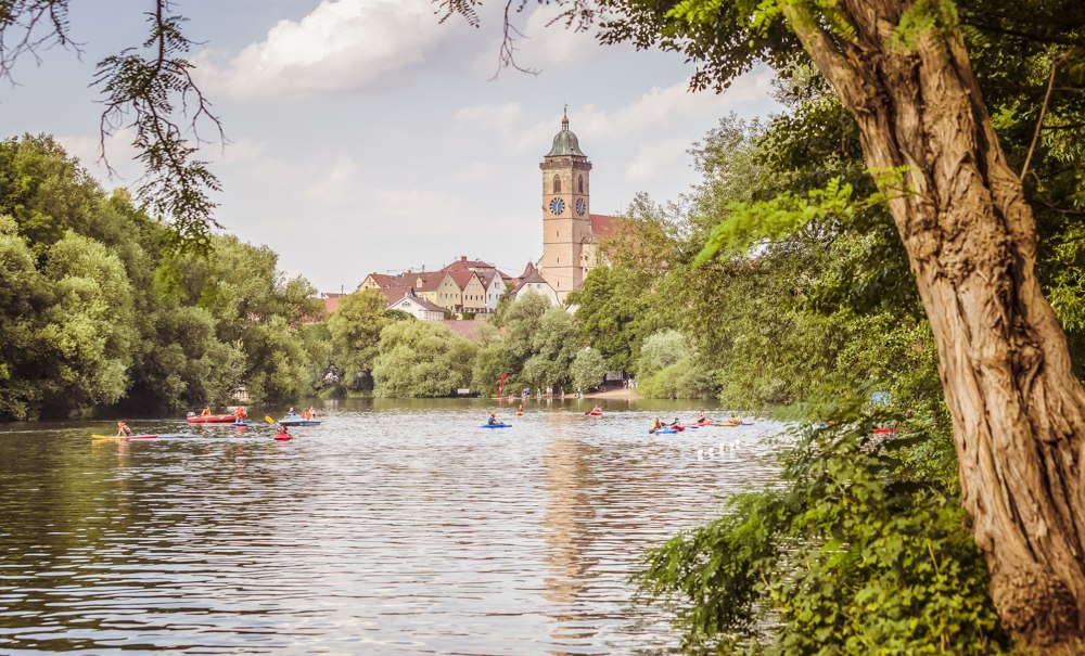 Ein Fluss mit Kanus, umgeben von Bäumen. Im Hintergrund ist ein Kirchturm und eine Stadt zu sehen., © Daniel Jüptner