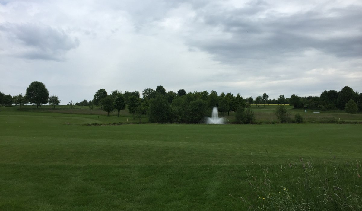 Weitl&auml;ufiger Golfplatz mit saftigem Gr&uuml;n, B&auml;umen und einem Springbrunnen. Der Himmel ist bew&ouml;lkt, was eine ruhige Atmosph&auml;re schafft., &copy; www.pro-cycl.de