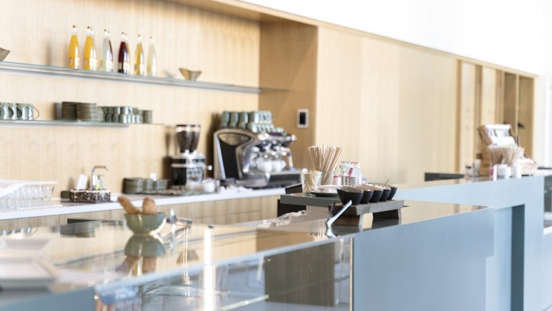 Modernes Caf&eacute; mit gl&auml;nzender Theke, Kaffeemaschine und Regalen mit Tassen und Flaschen an der Wand., &copy; Dominique Brewing