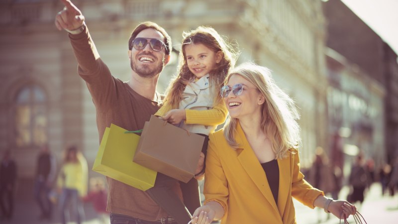 Eine fröhliche Familie mit Einkaufstüten genießt einen sonnigen Tag in der Stadt. Der Mann zeigt auf etwas in der Ferne. Eine fröhliche Familie mit Einkaufstüten genießt einen sonnigen Tag in der Stadt. Der Mann zeigt auf etwas in der Ferne.