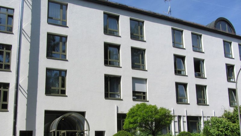 Mehrstöckiges Gebäude mit weißen Wänden und zahlreichen Fenstern, umgeben von Bäumen und Sträuchern., © Christkönigshaus Mehrstöckiges Gebäude mit weißen Wänden und zahlreichen Fenstern, umgeben von Bäumen und Sträuchern., © Christkönigshaus