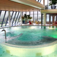 Modernes Schwimmbad mit großen Fenstern, grünem Wasser und Liegestühlen. Innenbereich mit Pflanzen und Sitzgelegenheiten., © Ufuk Arslan