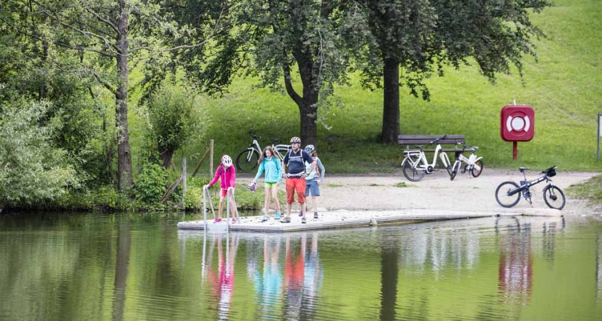 Eine Gruppe von Radfahrern steht auf einem Steg an einem See. Im Hintergrund sind Fahrräder, Bäume und eine Wiese zu sehen., © Schwäbische Alb Tourismusverband e.V. Eine Gruppe von Radfahrern steht auf einem Steg an einem See. Im Hintergrund sind Fahrräder, Bäume und eine Wiese zu sehen., © Schwäbische Alb Tourismusverband e.V.
