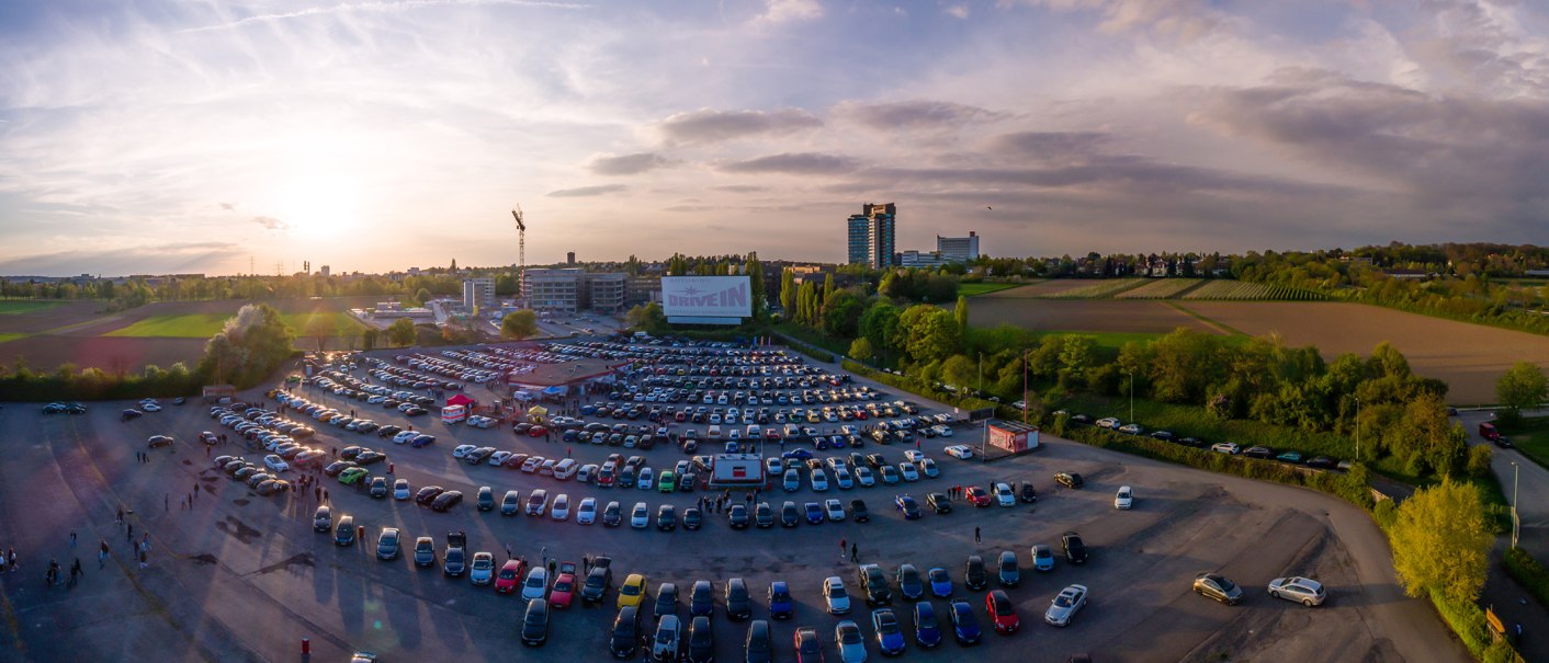 Luftaufnahme des Autokinos Kornwestheim bei Sonnenuntergang. Viele Autos sind geparkt, eine große Leinwand ist sichtbar. Im Hintergrund Felder und Gebäude., © DriveIn Autokinos DWJ GmbH Luftaufnahme des Autokinos Kornwestheim bei Sonnenuntergang. Viele Autos sind geparkt, eine große Leinwand ist sichtbar. Im Hintergrund Felder und Gebäude., © DriveIn Autokinos DWJ GmbH