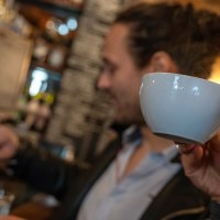 Zwei Personen in einem Café. Eine Person trinkt aus einer Tasse, während die andere Kaffee zubereitet. Im Hintergrund sind Regale mit Flaschen zu sehen., © Stuttgart Marketing  GmbH, Fotografin Martina Denker