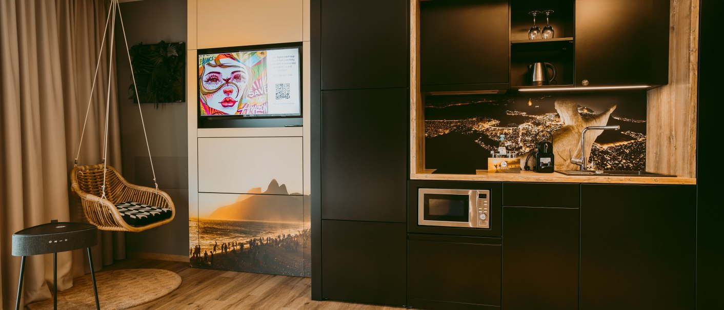Modernes Apartment mit Hängesessel, Fernseher, stilvoller Küchenzeile und Holzboden. Dekorative Wandbilder und gemütliche Atmosphäre., © Rioca Stuttgart Posto 4 GmbH