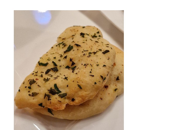 Zwei Stücke indisches Fladenbrot, bestreut mit Kräutern, liegen auf einem weißen Teller. Das Brot wirkt frisch und aromatisch., © Kultweine-Kochwelten-Kunstücke - Kochschule Sonja Lenz Zwei Stücke indisches Fladenbrot, bestreut mit Kräutern, liegen auf einem weißen Teller. Das Brot wirkt frisch und aromatisch., © Kultweine-Kochwelten-Kunstücke - Kochschule Sonja Lenz