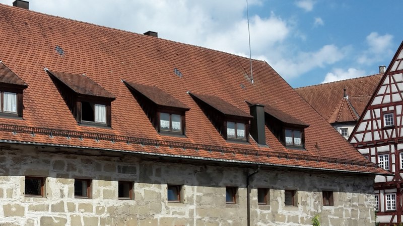 langestrecktes Steingebäude mit kleinen Fenstern und rotbraunem Ziegeldach mit mehreren Dachgauben, im Hintergrund rechts der Fachwerkgiebel des Alten Schlosses mit braunem Holz und weißen Gefachen, © Stadt Gaildorf langestrecktes Steingebäude mit kleinen Fenstern und rotbraunem Ziegeldach mit mehreren Dachgauben, im Hintergrund rechts der Fachwerkgiebel des Alten Schlosses mit braunem Holz und weißen Gefachen, © Stadt Gaildorf